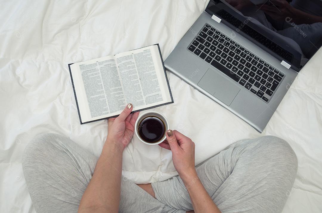 Mulher com pernas cruzadas, lendo livro e bebendo café, compu