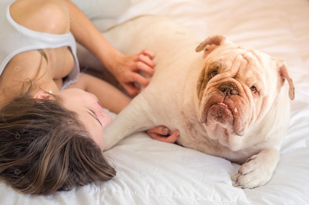 Linda mulher dormindo na cama com cachorro bulldog inglês.