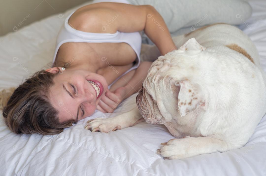 Linda mulher dormindo na cama com cachorro bulldog inglês.