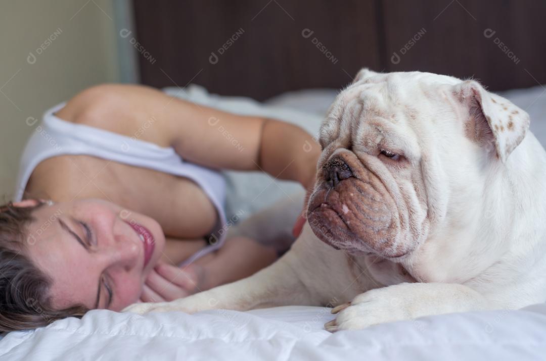 Linda mulher dormindo na cama com cachorro bulldog inglês.