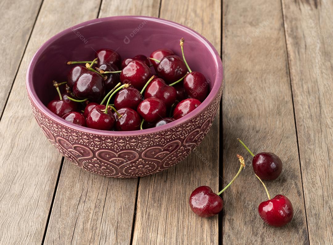 Cerejas vermelhas em uma tigela sobre mesa de madeira.