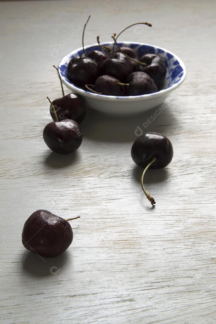 Cerejas pretas em uma tigela vintage branca e azul sobre mesa de madeira.