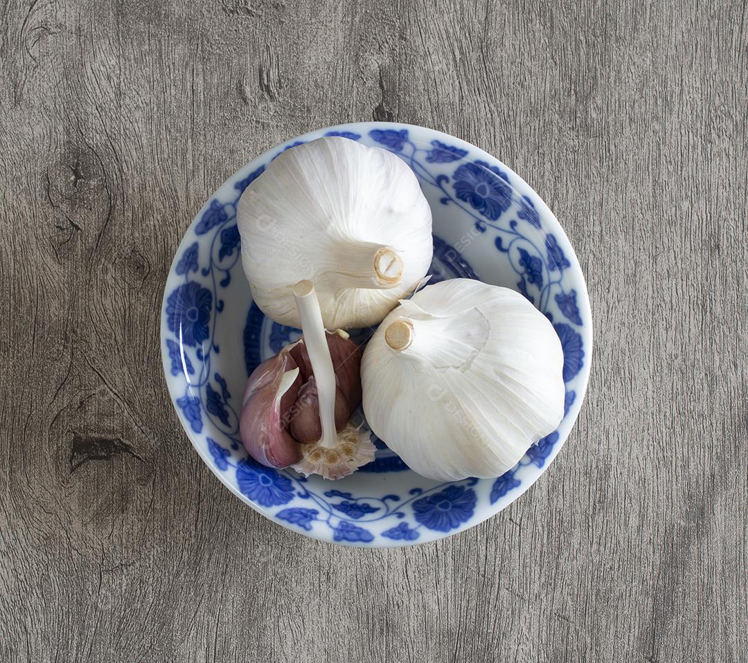 alho e cravo em uma tigela branca e azul decorada sobre fundo de madeira.