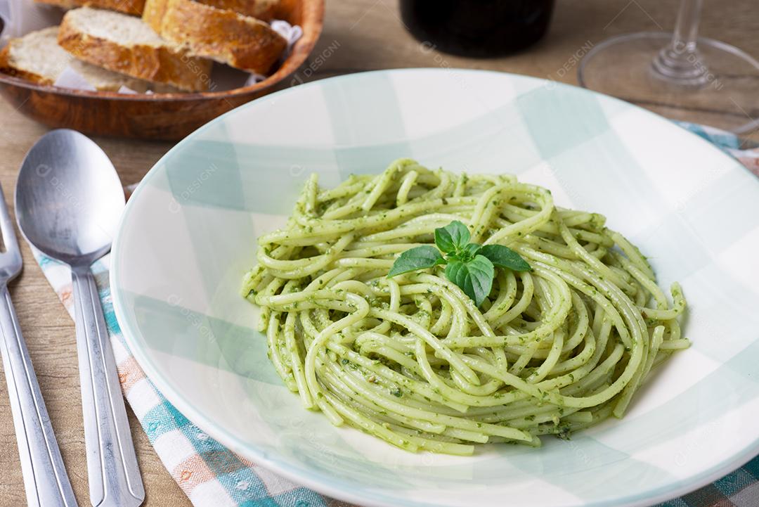 Espaguete com pesto em um prato branco e verde com pão e uma taça de vinho.