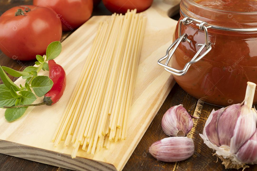 Espaguete, tomate, alho, pimentas e ervas sobre a mesa de madeira.