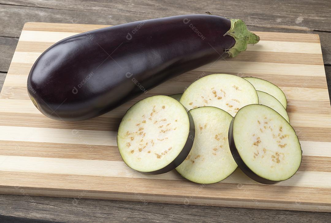 Berinjela crua com fatias sobre tábua de madeira.