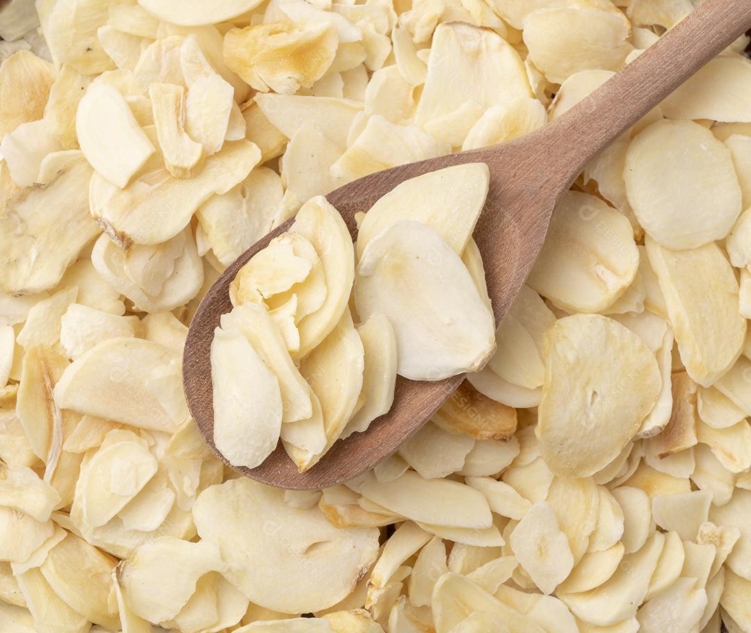 Vista superior, fatias de alho seco em uma colher de madeira. Pano de fundo da comida.