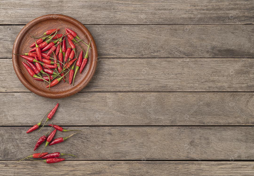 Pimentas malagueta vermelhas em um prato sobre mesa de madeira