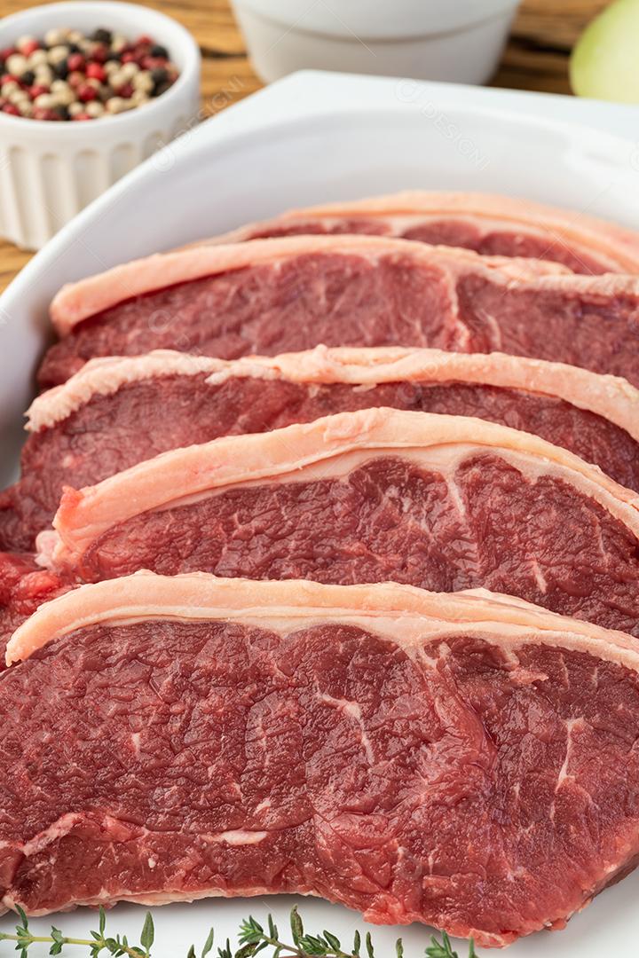 Carne de lombo de tira crua fatiada sobre prato branco com temperos.