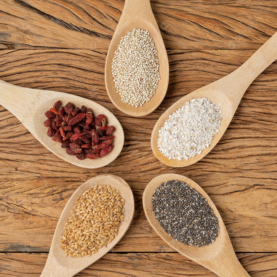 Super alimentos variados em colheres sobre mesa de madeira. Chia, quinoa, aveia, linhaça