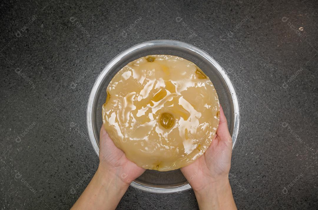 Mão segurando o cogumelo de chá kombucha scoby contra fundo de pedra com tigela