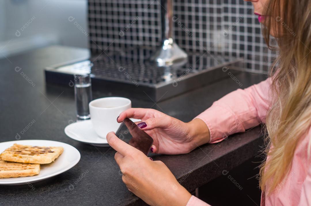 Jovem mulher usando smartphone bebendo café, café da manhã.