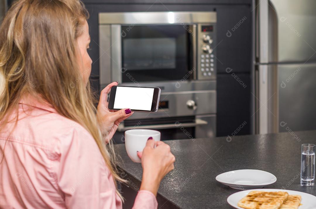 Jovem mulher usando smartphone bebendo café, café da manhã.