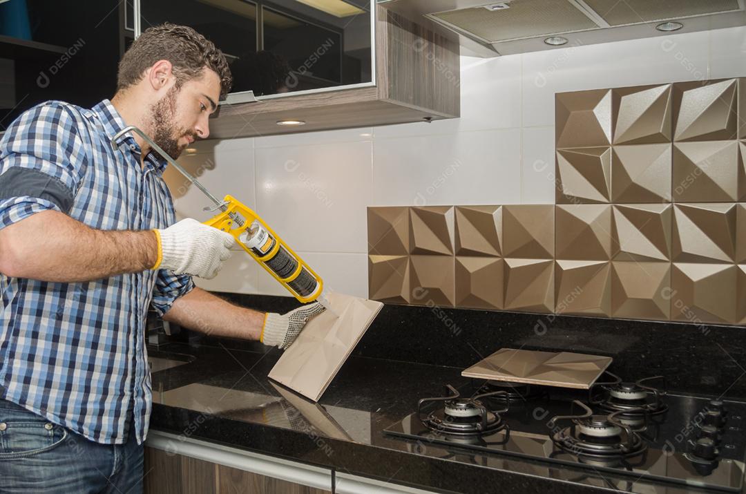 Homem reformando, reformando a cozinha, instalando azulejo na parede.