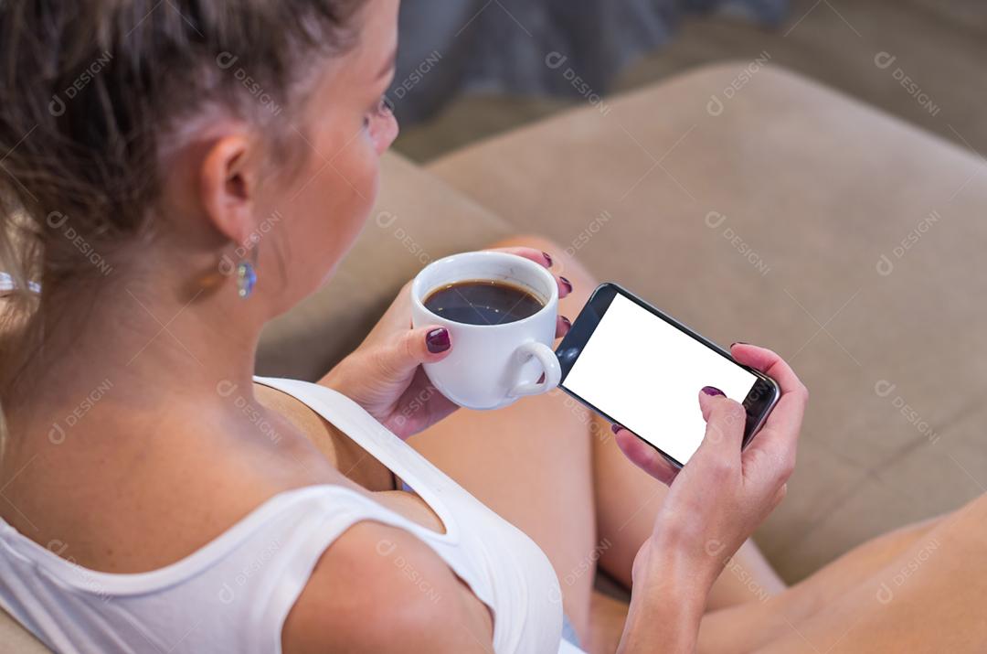 Jovem mulher usando smartphone bebendo café da manhã.