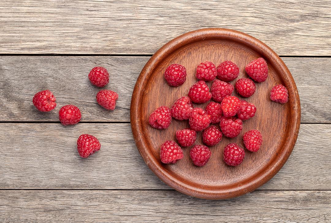 Framboesas em um prato sobre mesa de madeira.