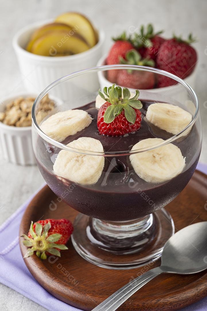 Tigela de açaí típica brasileira com frutas e muesli sobre fundo de madeira.