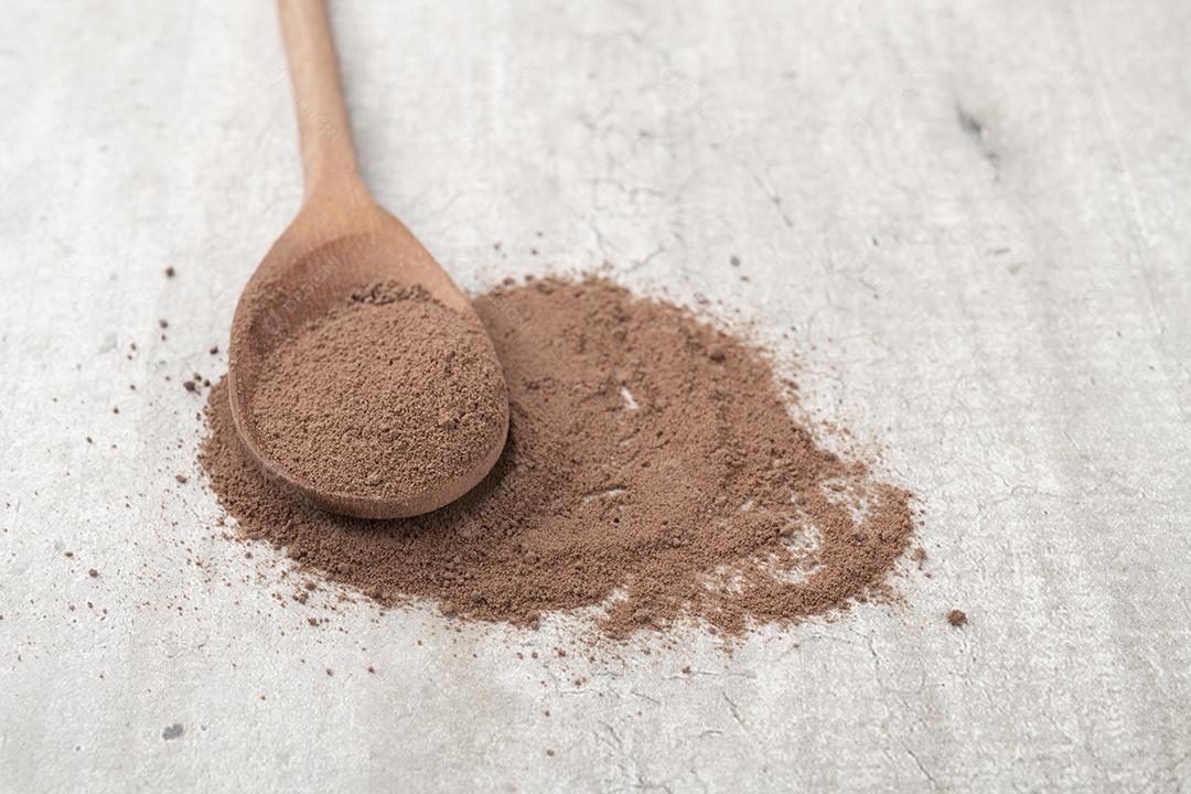 Cacau em pó em uma colher de madeira sobre fundo rústico.