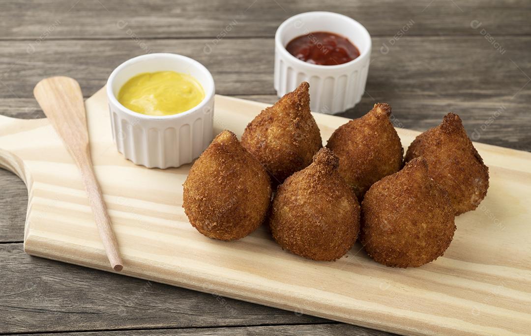 Coxinha típica brasileira de lanche em uma tábua de madeira com ketchup e mostarda.