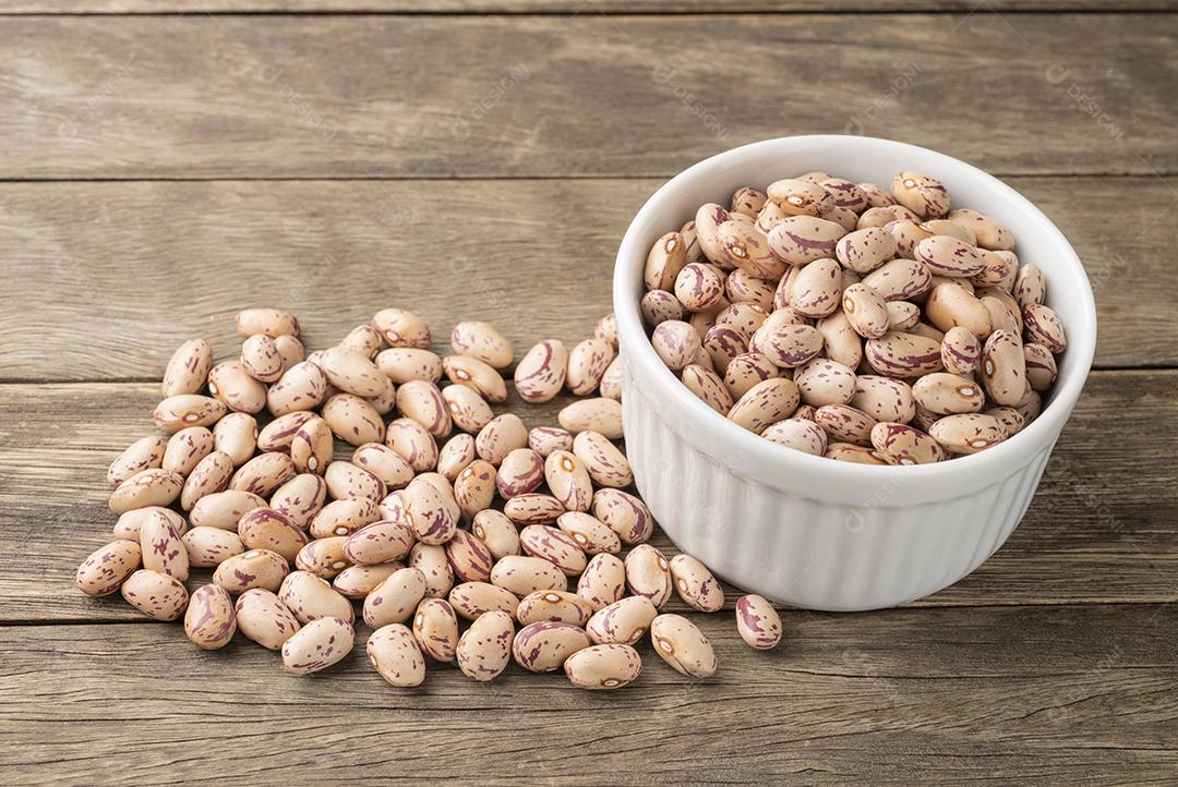 Feijões marrons em uma tigela sobre mesa de madeira.