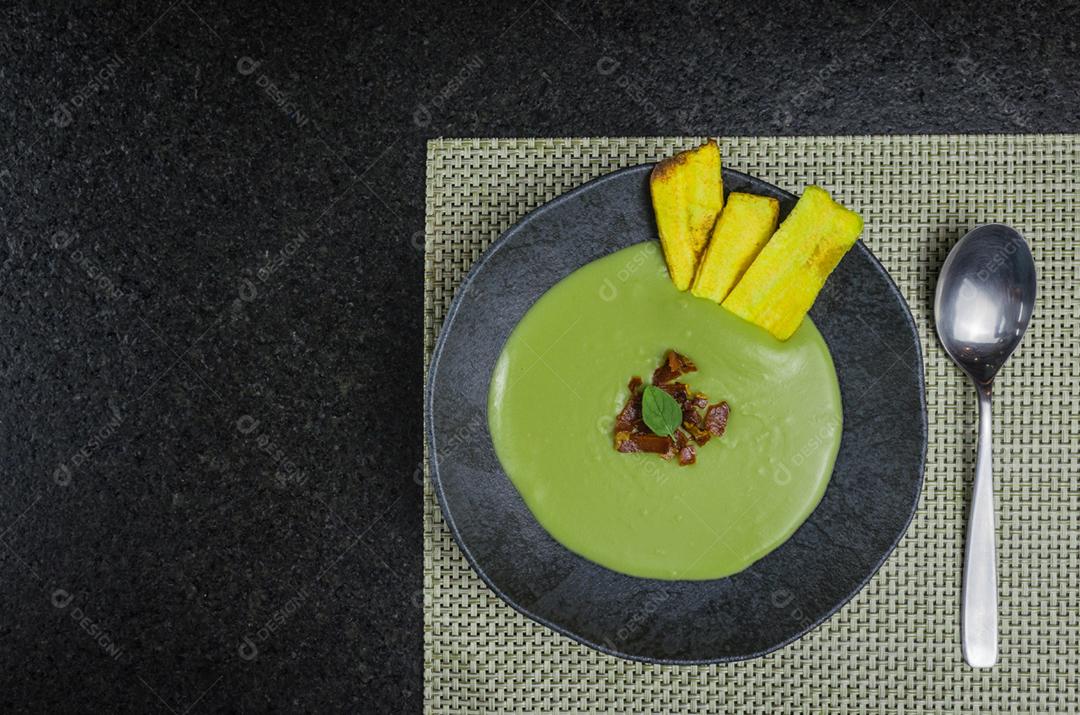 Delicioso creme de ervilha de bacon com chips de banana em um lindo prato de ardósia.