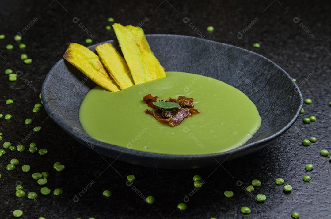 Delicioso creme de ervilha de bacon com chips de banana em um lindo prato de ardósia.