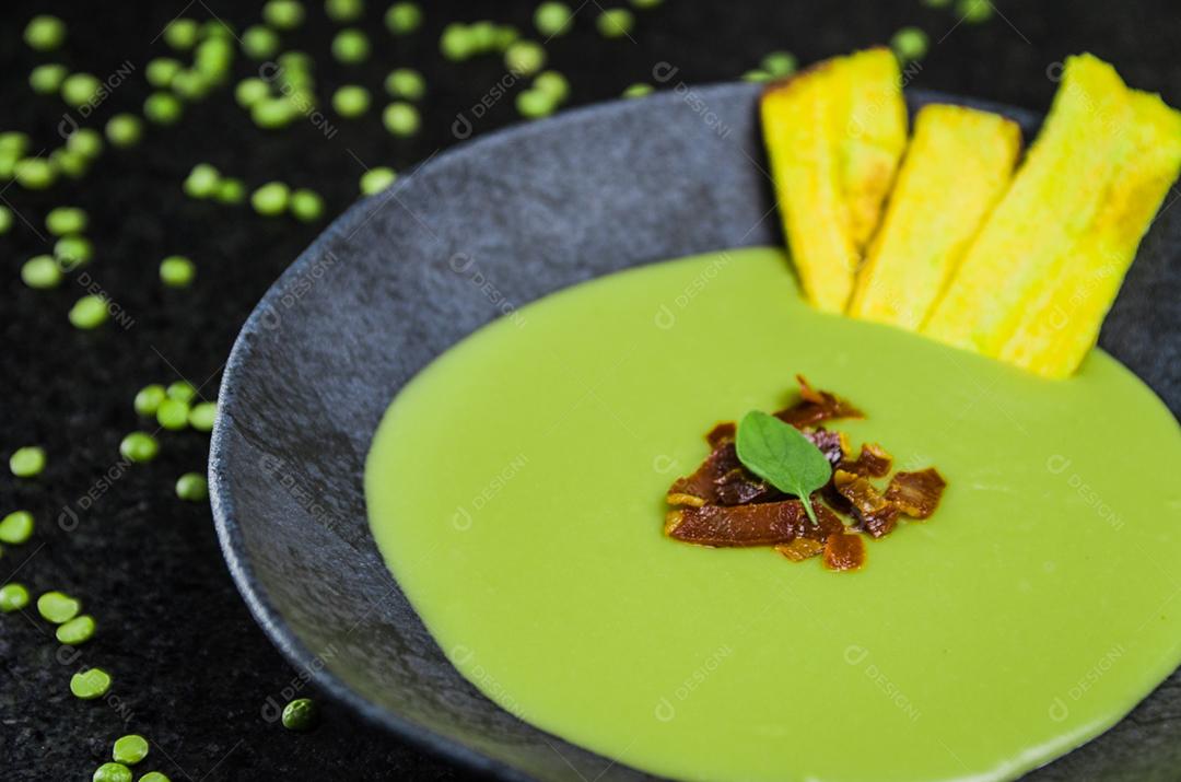 Delicioso creme de ervilha de bacon com chips de banana em um lindo prato de ardósia.