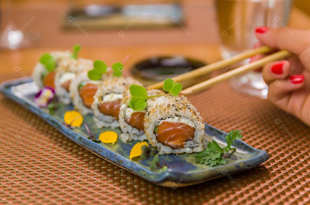 Mulher comendo delicioso sushi gunkan, closeup em pauzinhos