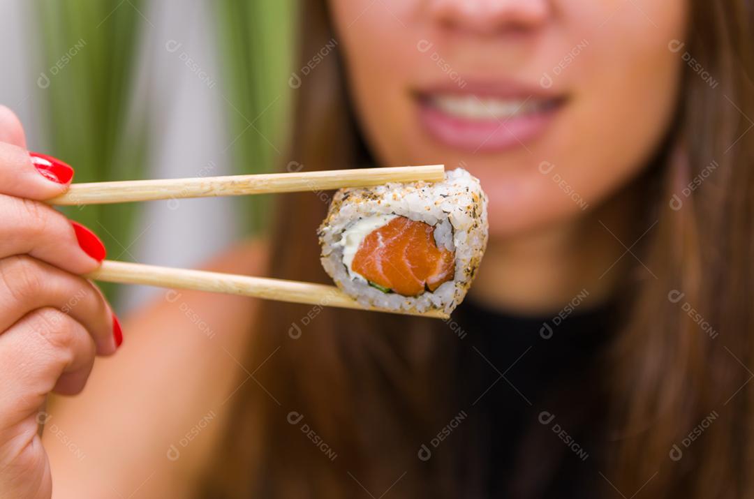 Mulher comendo delicioso sushi gunkan, closeup em pauzinhos