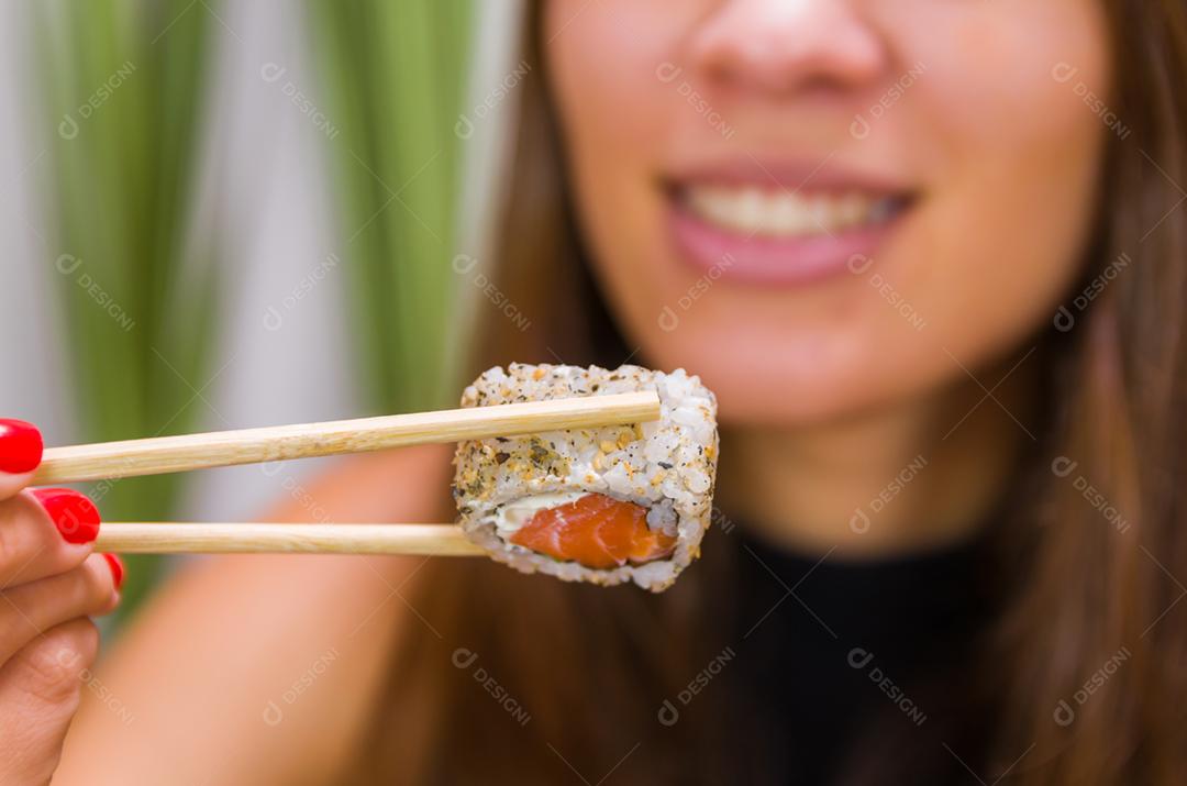 Mulher comendo delicioso sushi gunkan, closeup em pauzinhos