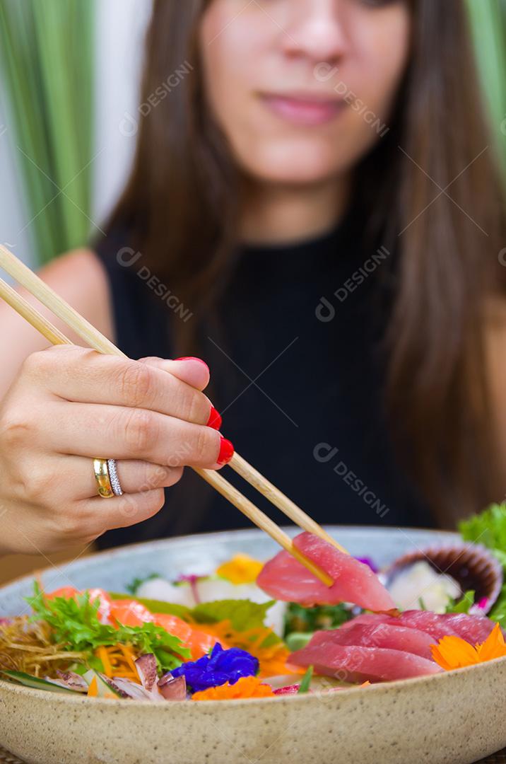 Mulher comendo delicioso sashimi, closeup em pauzinhos.