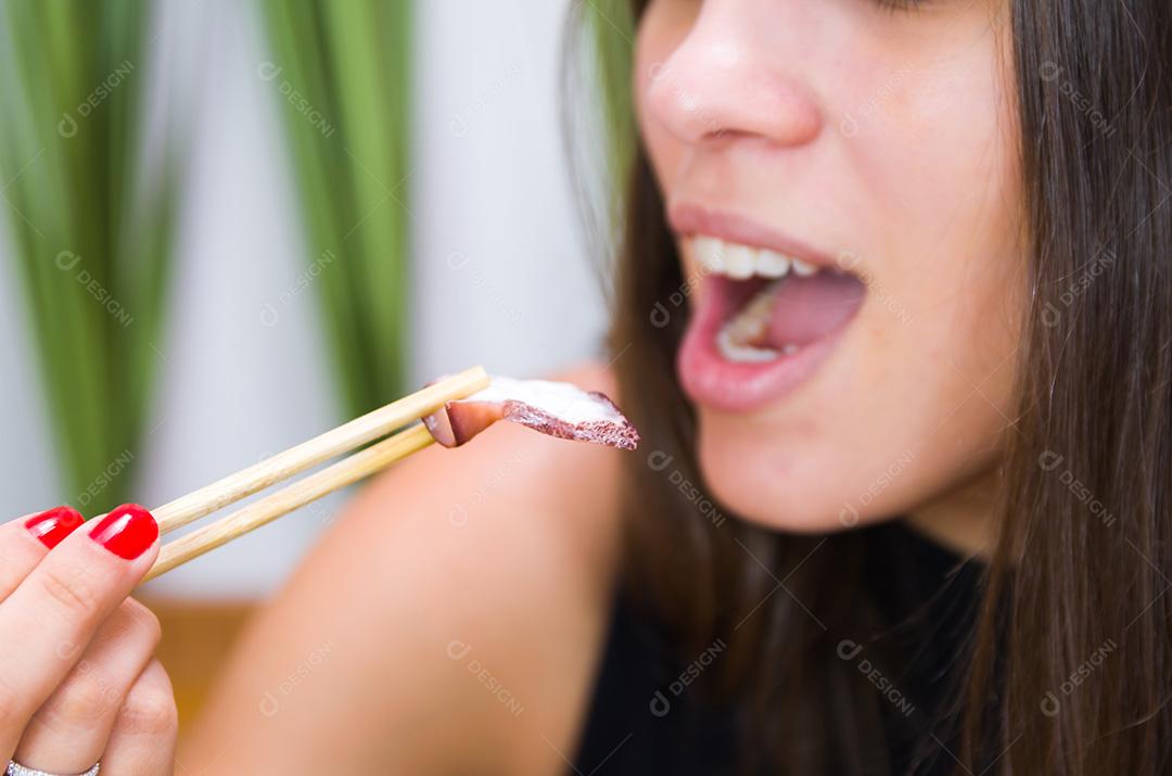Mulher comendo delicioso sashimi, closeup em pauzinhos.