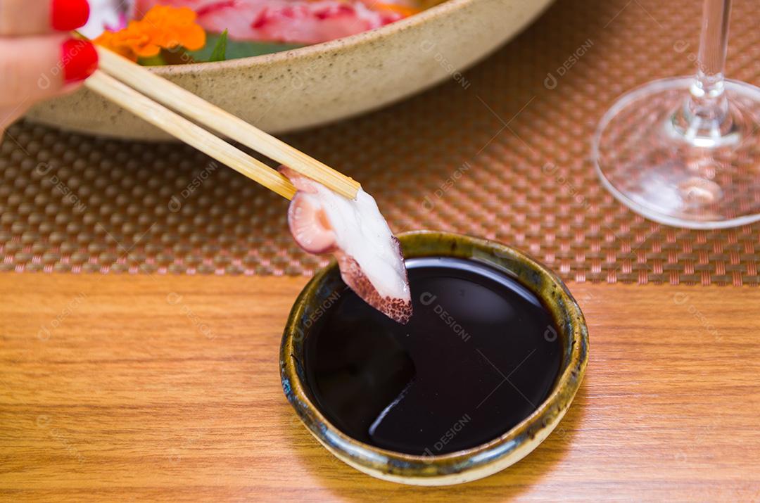 Mulher comendo delicioso sashimi, closeup em pauzinhos.