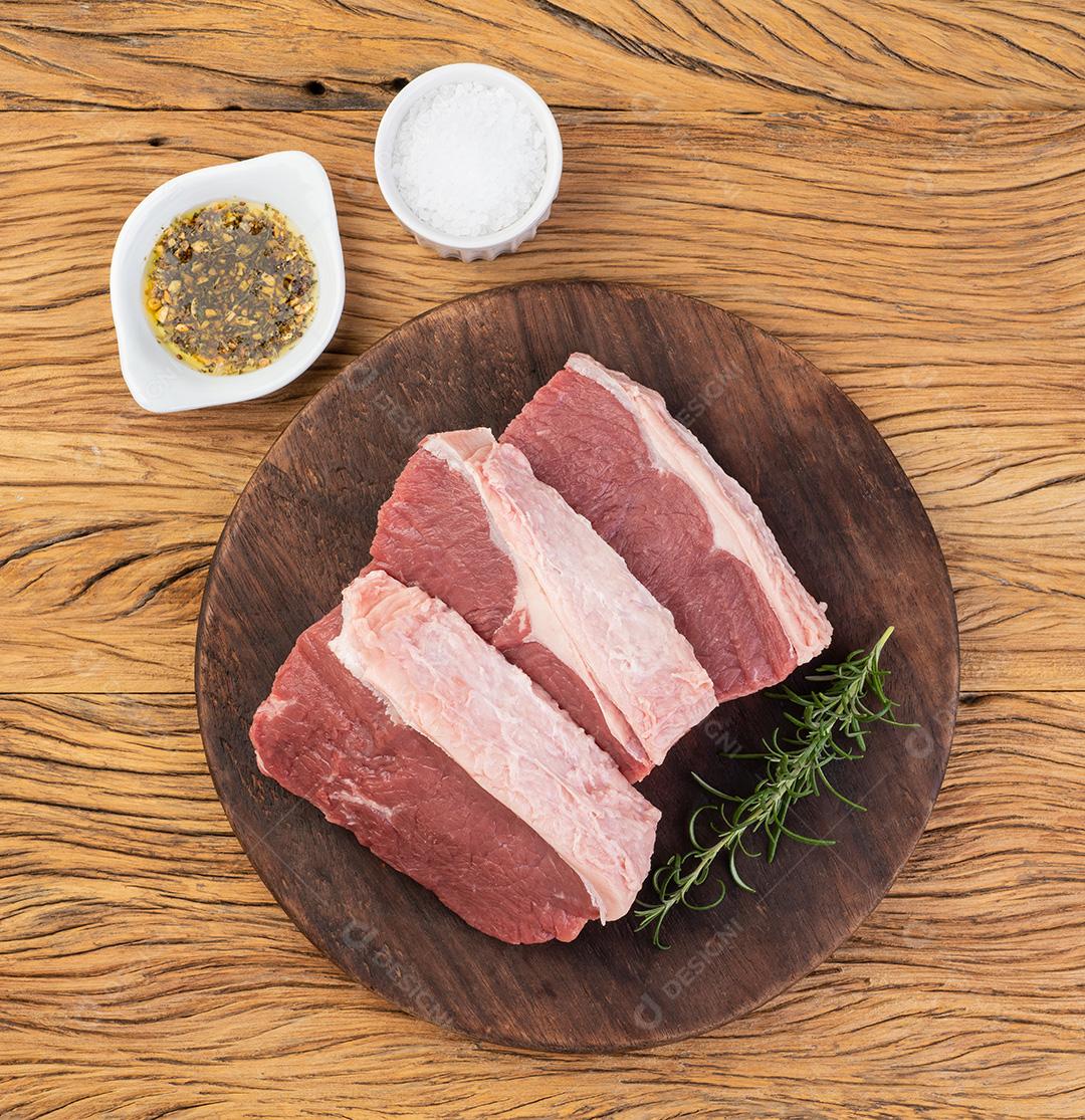 Carne de ancho cru fatiada, corte típico argentino, sobre tábua de madeira com temperos.