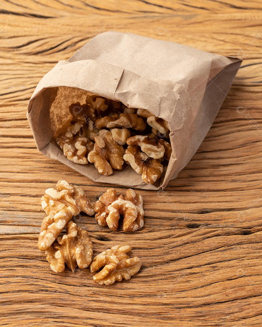Nozes em um saco de papel sobre mesa de madeira.