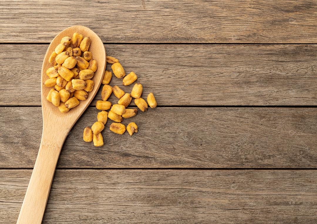 Milho frito em uma colher sobre mesa de madeira