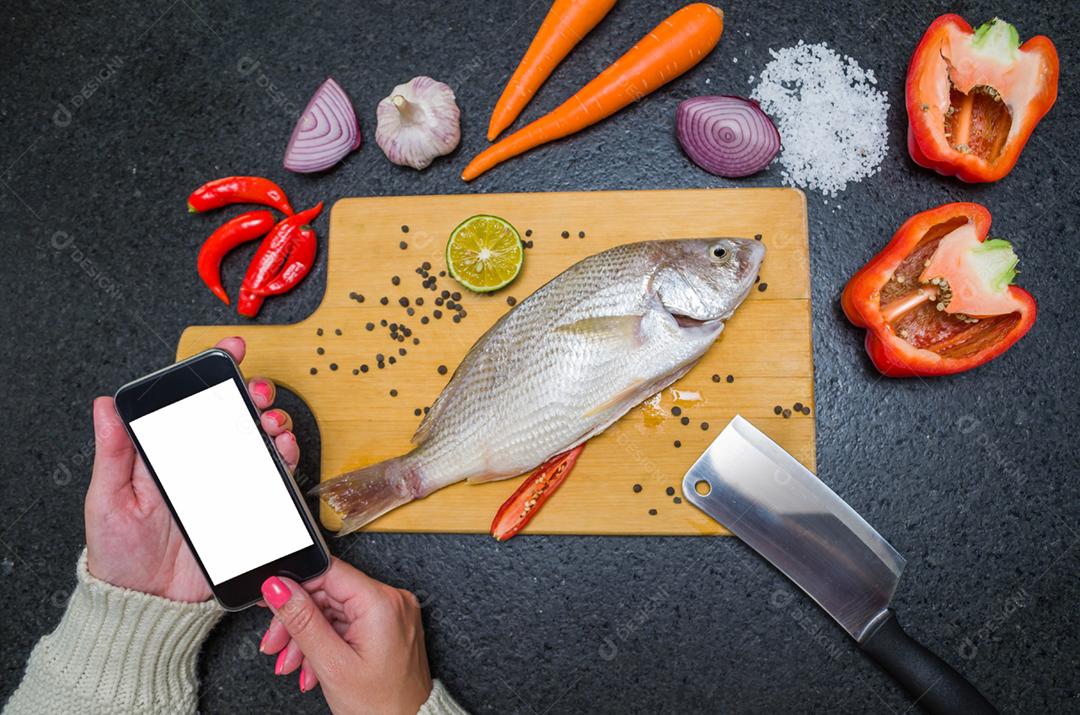 Preparando um prato gastronômico de corvina assada, a jovem consultou o livro de receitas