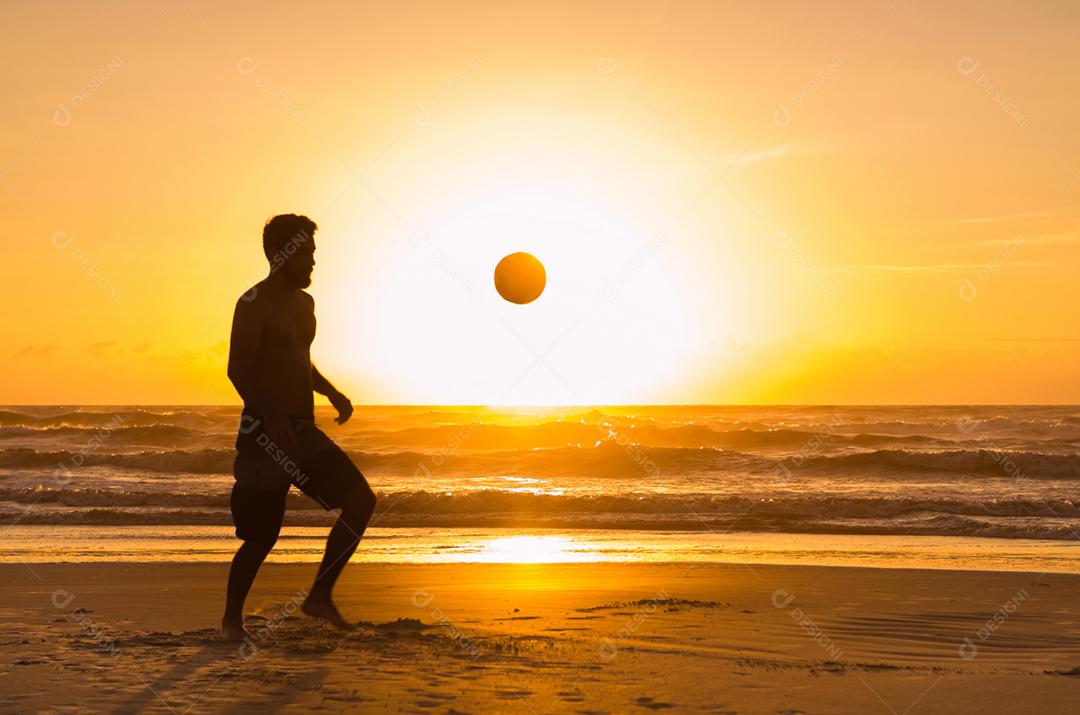 Grande conceito de futebol, homem jogando futebol na praia na hora dourada, pôr do sol