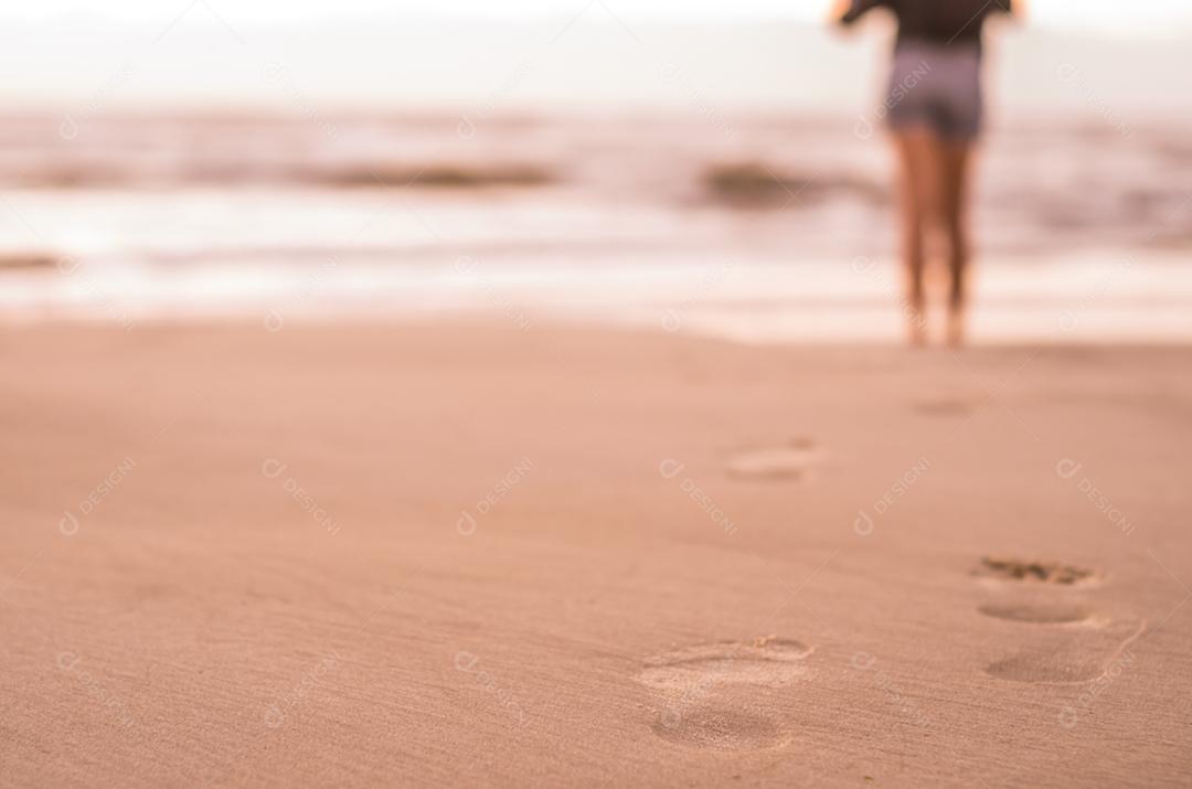 Mulher andando na praia, pegadas na areia.