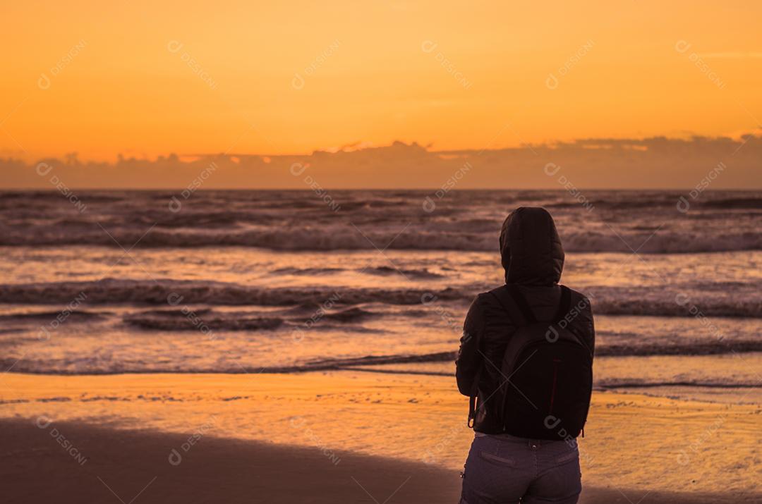 Mulher olhando para o horizonte, praia ao pôr do sol