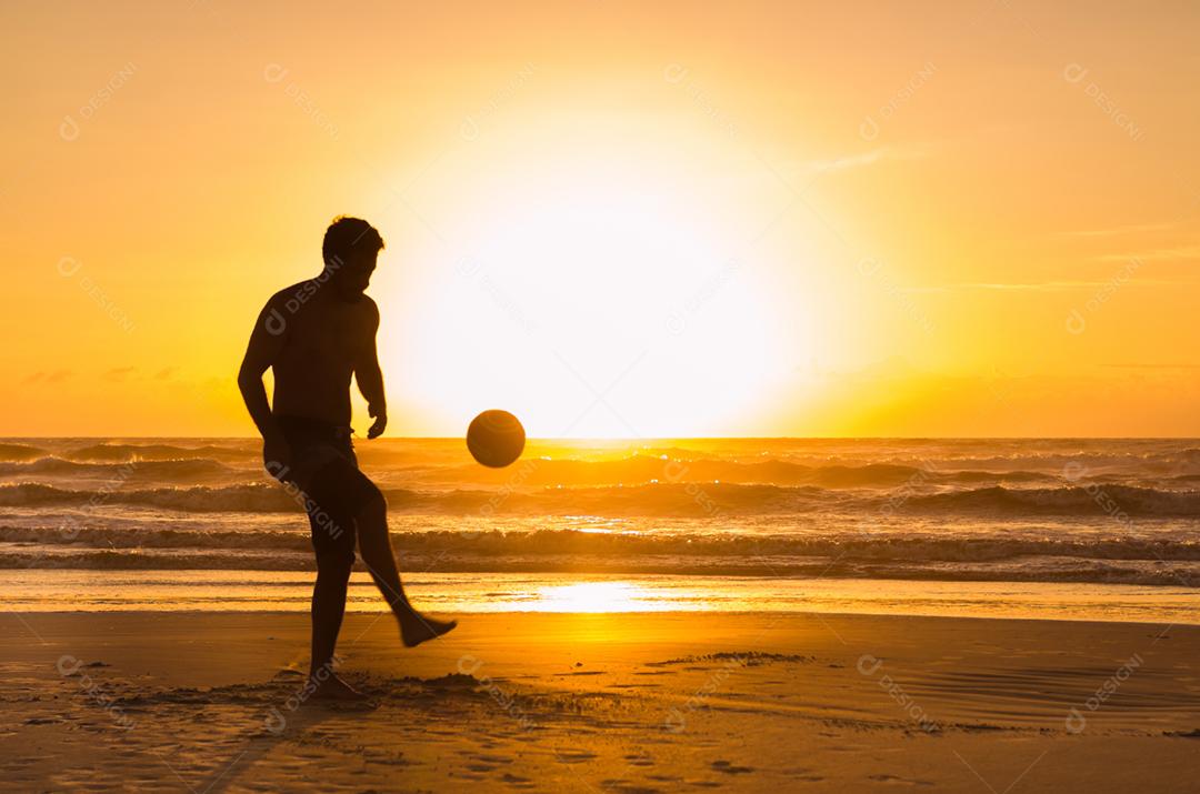 Grande conceito de futebol, homem jogando futebol na praia na hora dourada, pôr do sol