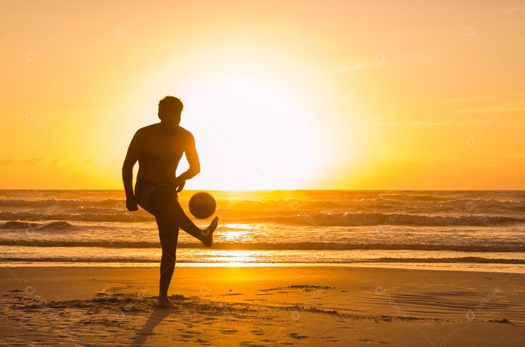 Grande conceito de futebol, homem jogando futebol na praia na hora dourada, pôr do sol
