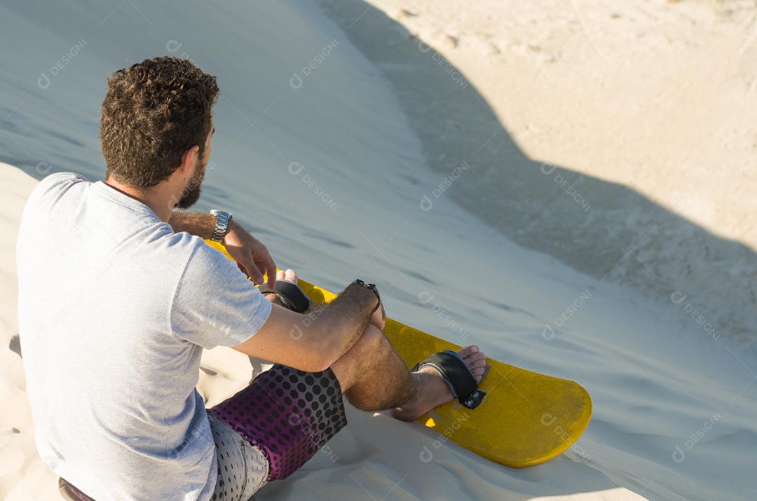 Jovem de costas olhando para as dunas de areia, preparando-se para praticar sandboard.