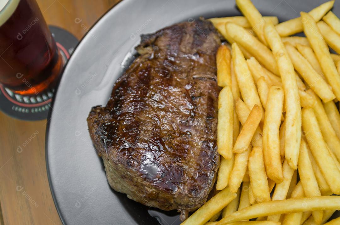 Delicioso prato de entrecosto grelhado com batatas fritas e copo de cerveja