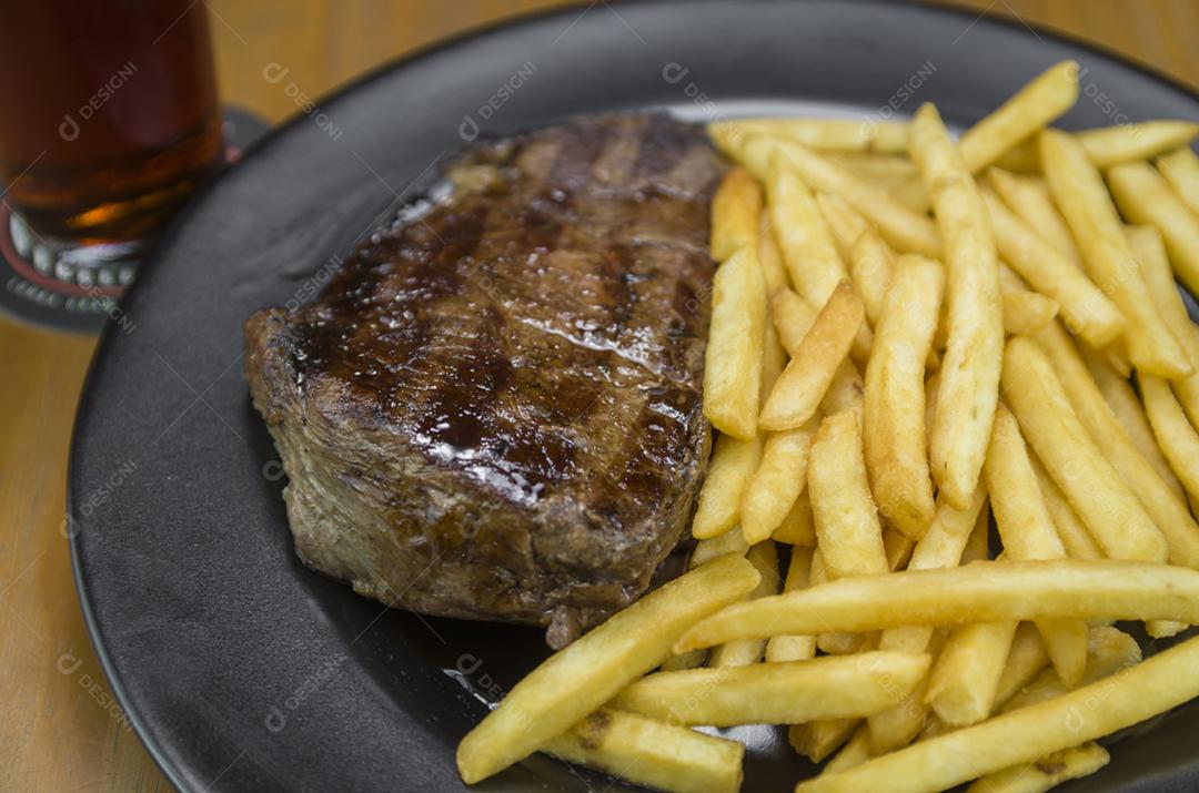 Delicioso prato de entrecosto grelhado com batatas fritas e copo de cerveja