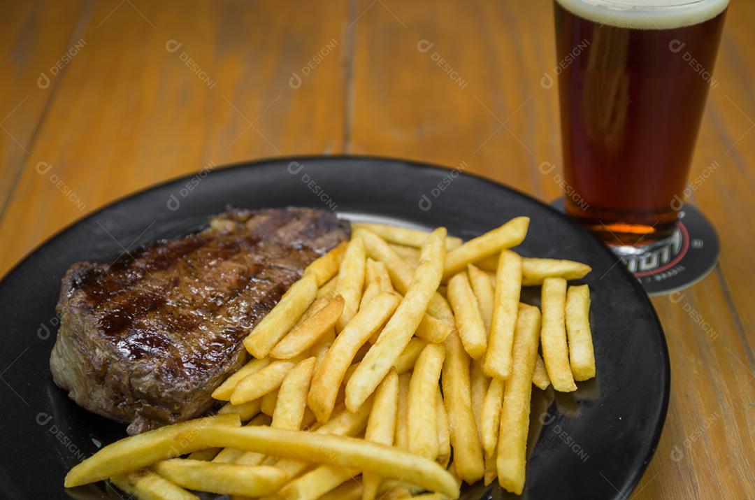 Delicioso prato de entrecosto grelhado com batatas fritas e copo de cerveja