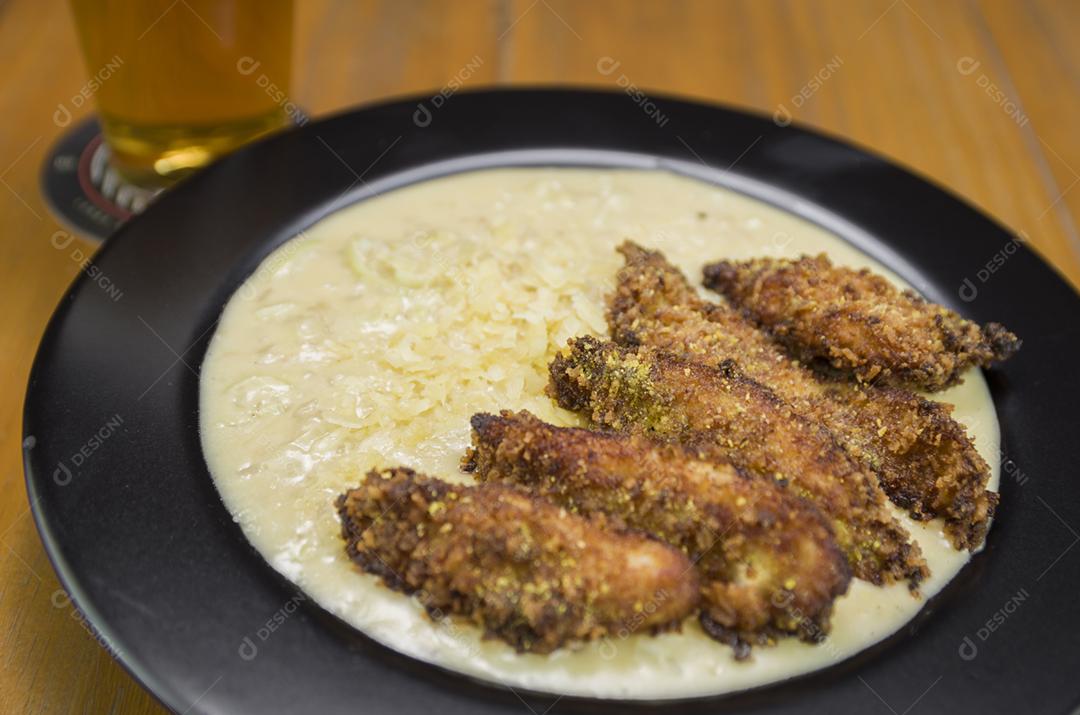 Delicioso prato de risoto de frango com pedaços de peito de frango à milanesa em um prato preto.