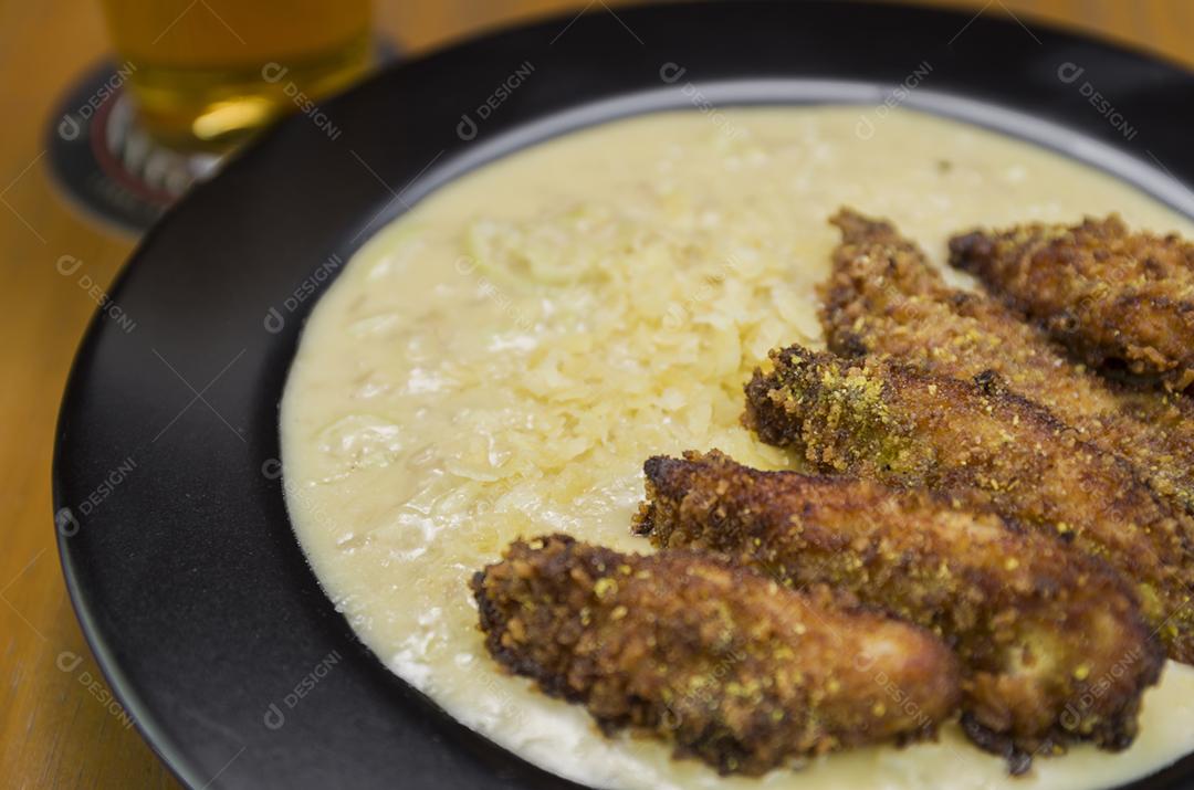 Delicioso prato de risoto de frango com pedaços de peito de frango à milanesa em um prato preto.