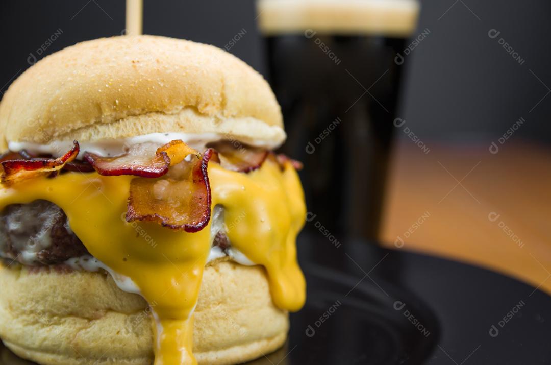 Hambúrguer de bacon caseiro e molho cheddar na mesa de madeira e fundo preto