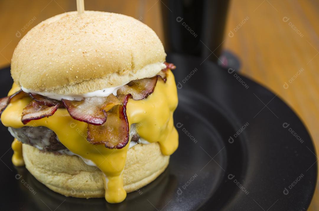 Hambúrguer de bacon caseiro e molho cheddar na mesa de madeira e fundo preto